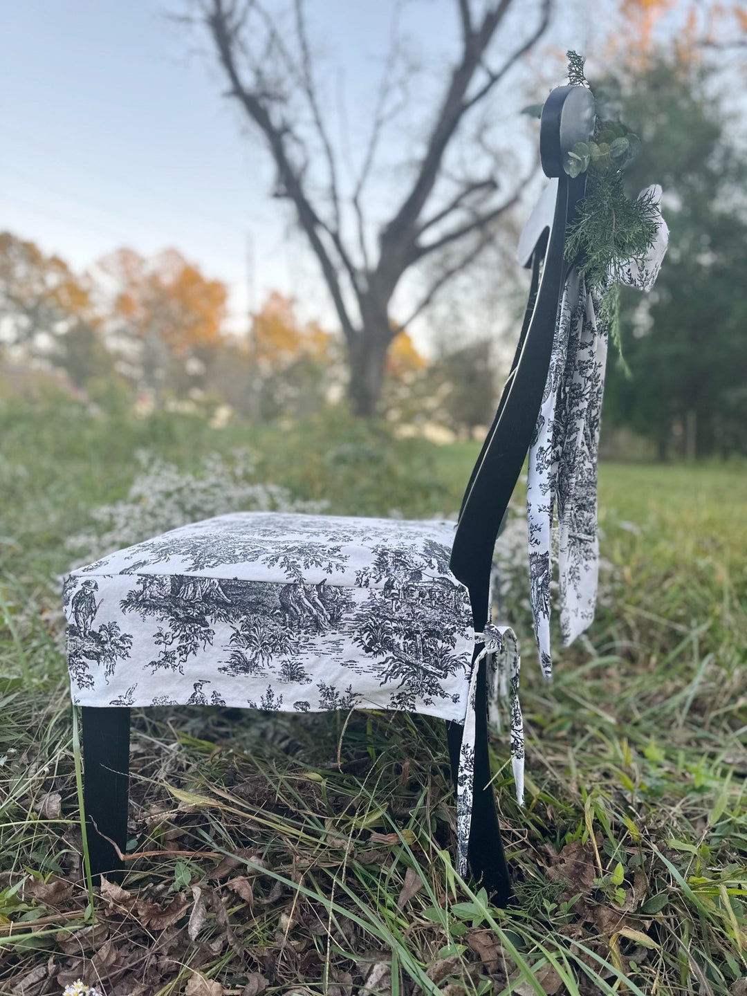 Profile of a black dining chair dressed in a toile seat slipcover with a toile sash bow on the back