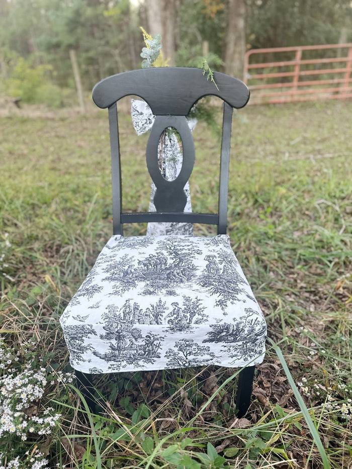 Black toile tailored chair seat slipcover on a black dining chair, front view, in a field of white asters