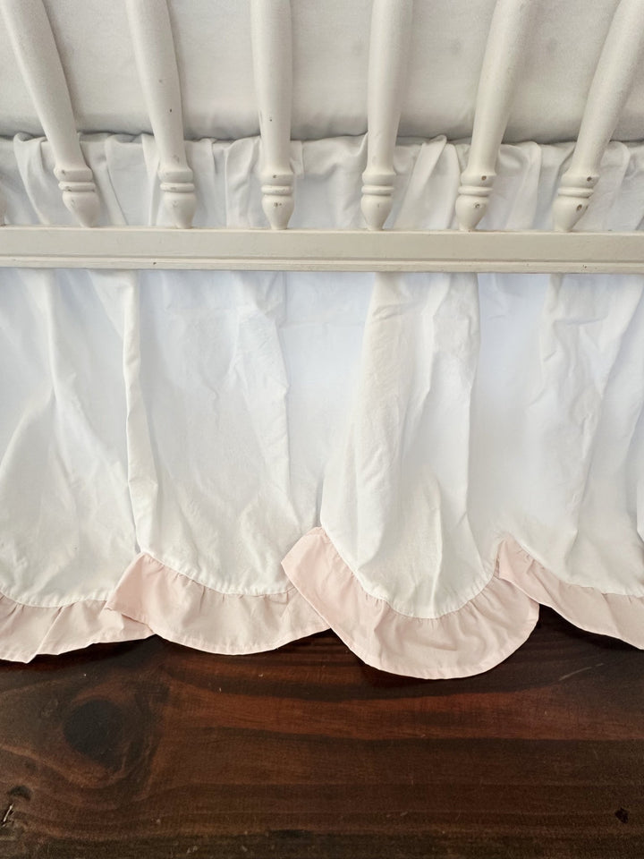 Close view of the scalloped hem and its baby pink ruffle curving beneath the crib rail