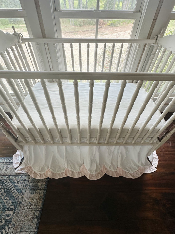 Overhead front view of the crib showing the scalloped hem and pink ruffle across the front panel