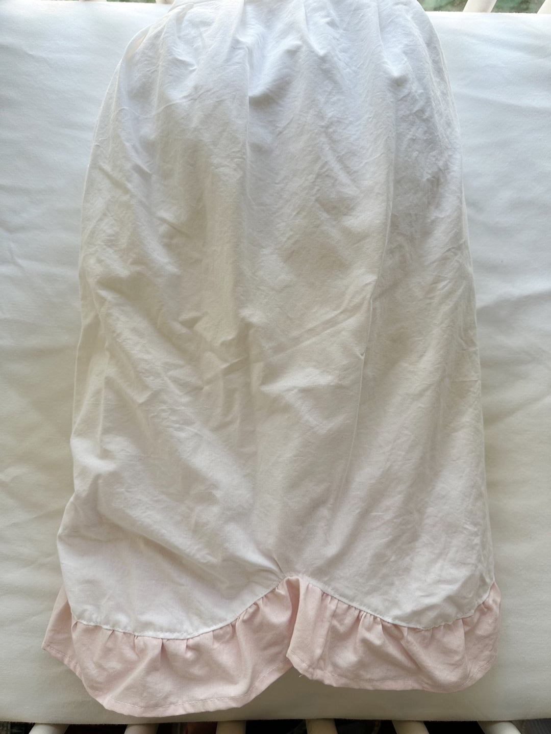 One panel of the crib skirt laid flat over the crib rail showing the scallop shape and pink ruffle edge