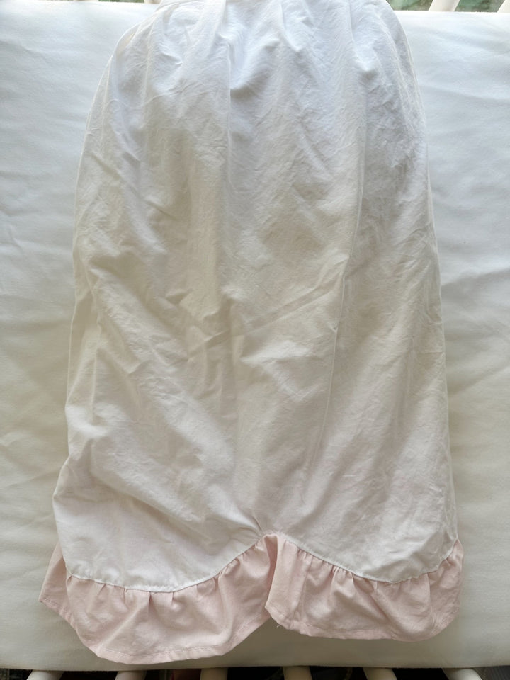One panel of the crib skirt laid flat over the crib rail showing the scallop shape and pink ruffle edge