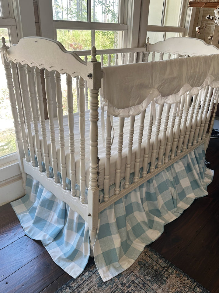 Angled view of the two piece blue buffalo check crib bedding set with white ruffled scalloped rail cover