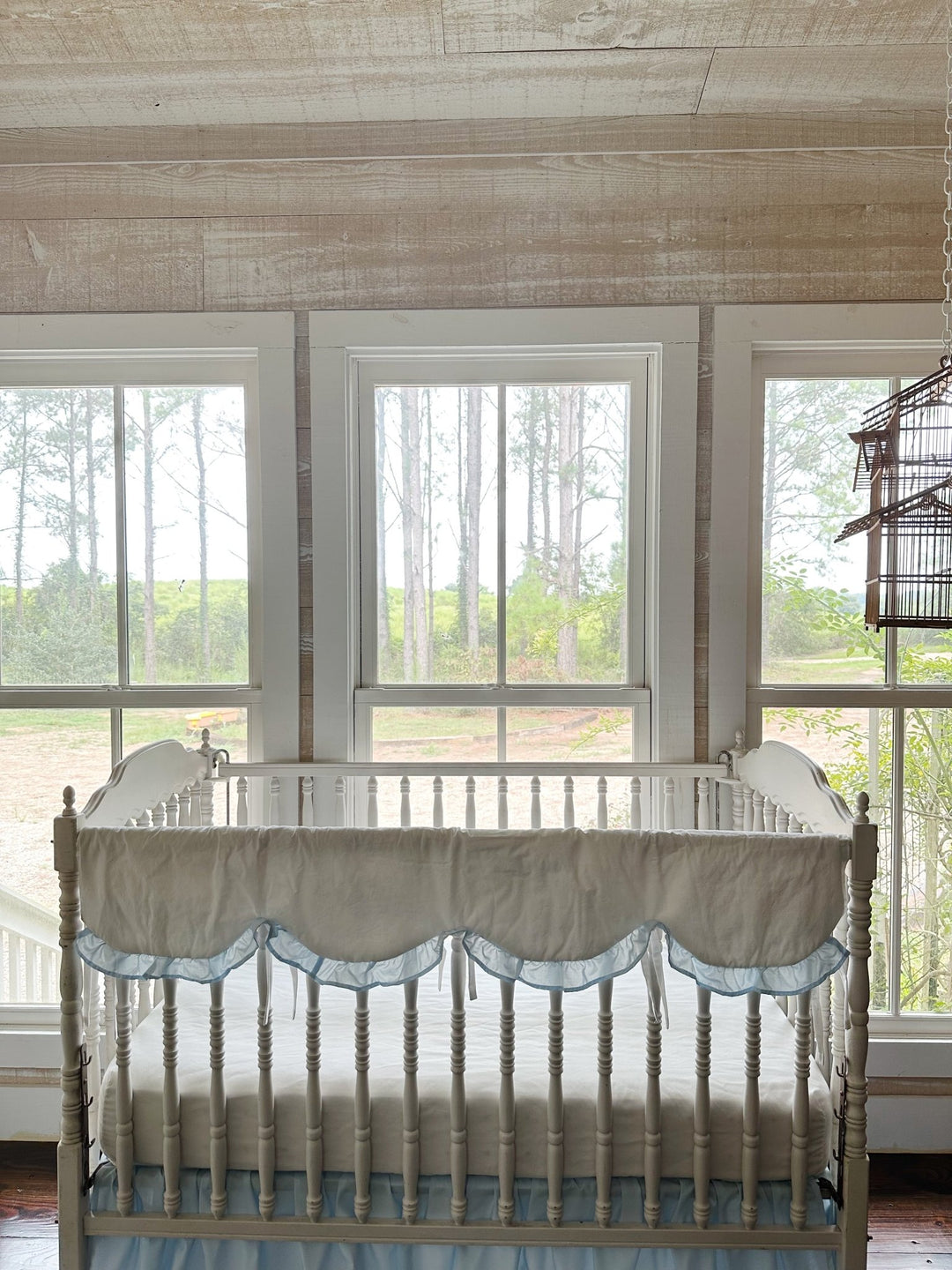 Wide nursery view with the scalloped rail cover on the crib beneath three bright windows