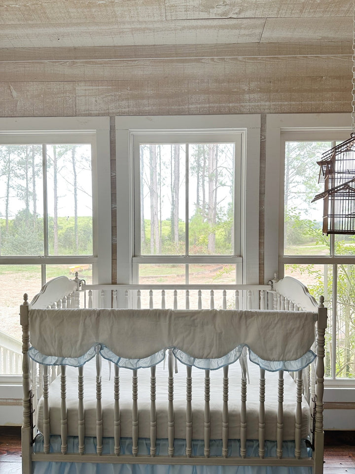 Wide nursery view with the scalloped rail cover on the crib beneath three bright windows