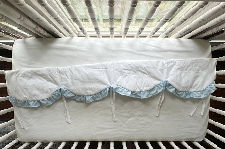 The white scalloped rail cover folded to show its heirloom blue ruffle trim and slim white ties