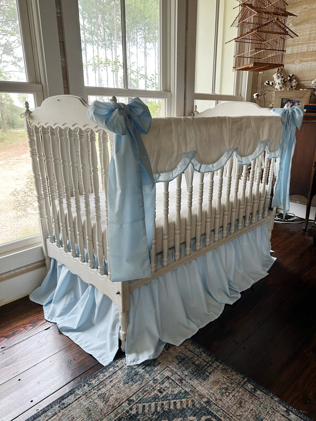 Angled view of the heirloom blue crib bedding set showing the skirt gathers and a bow tied at the corner post