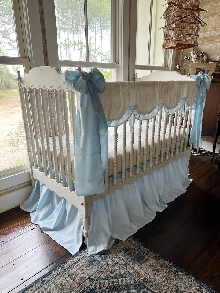 Angled view of the heirloom blue crib bedding set showing the skirt gathers and a bow tied at the corner post