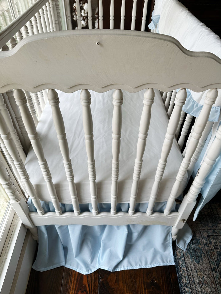 Looking into the crib from the end over a white fitted sheet with the heirloom blue skirt below