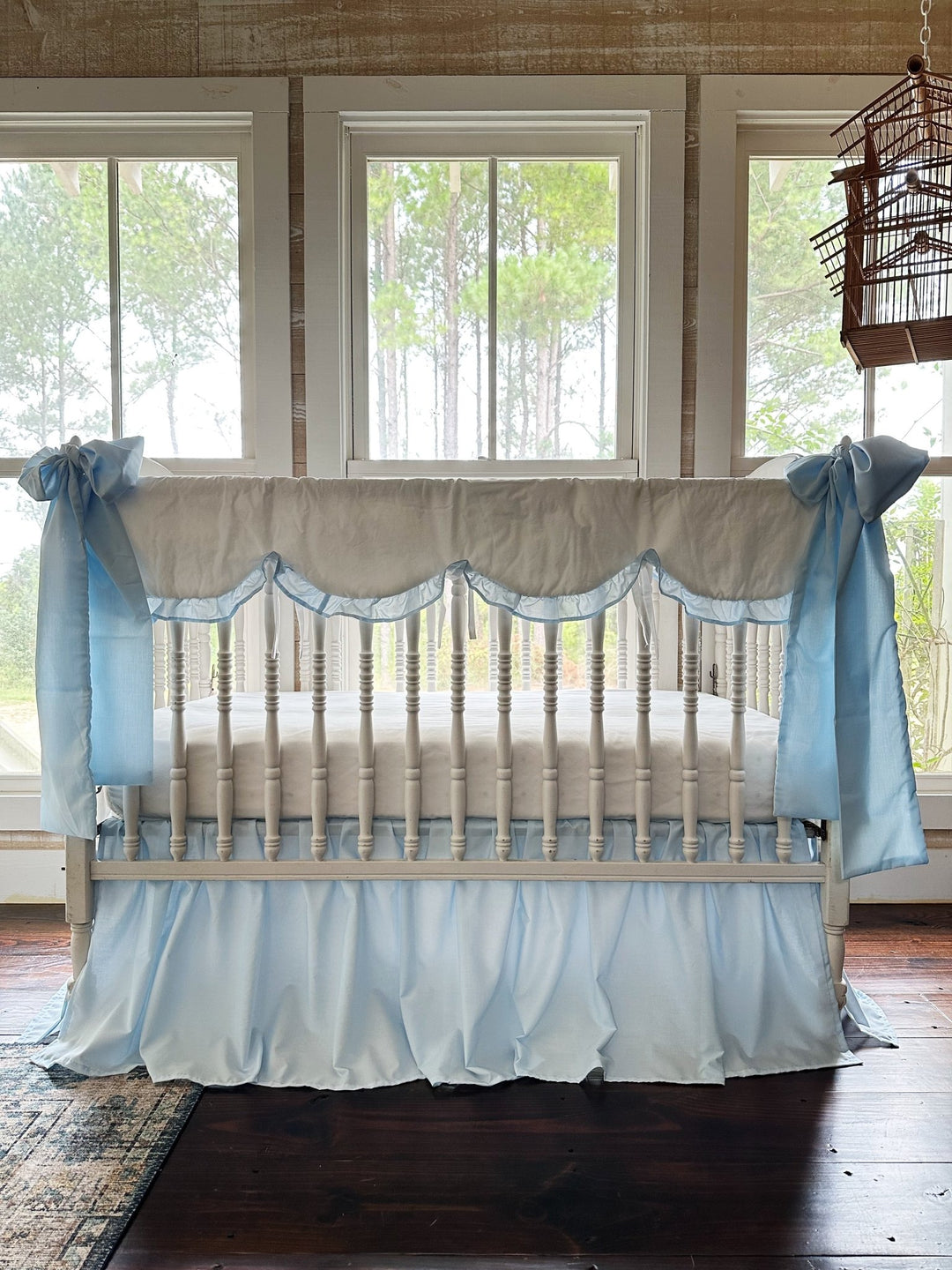 White scalloped crib rail cover with heirloom blue ruffle, blue farmhouse skirt and two large blue bows on a white spindle crib