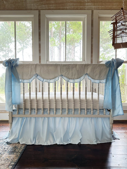 White scalloped crib rail cover with heirloom blue ruffle, blue farmhouse skirt and two large blue bows on a white spindle crib