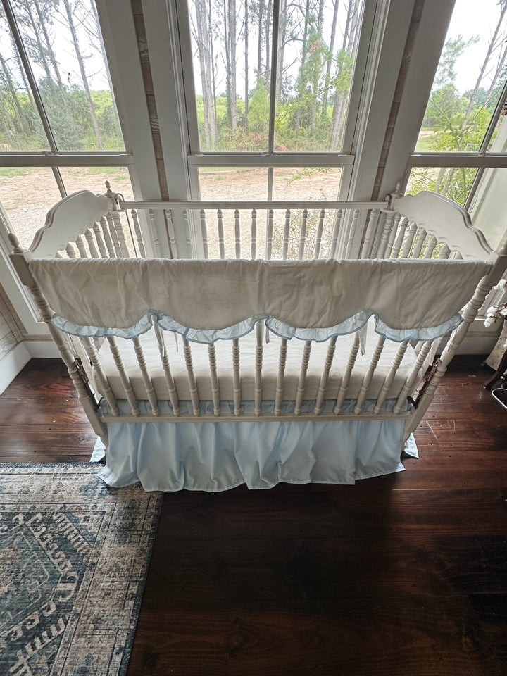 Raised view of the crib with the scalloped cover across the front rail and blue skirt below