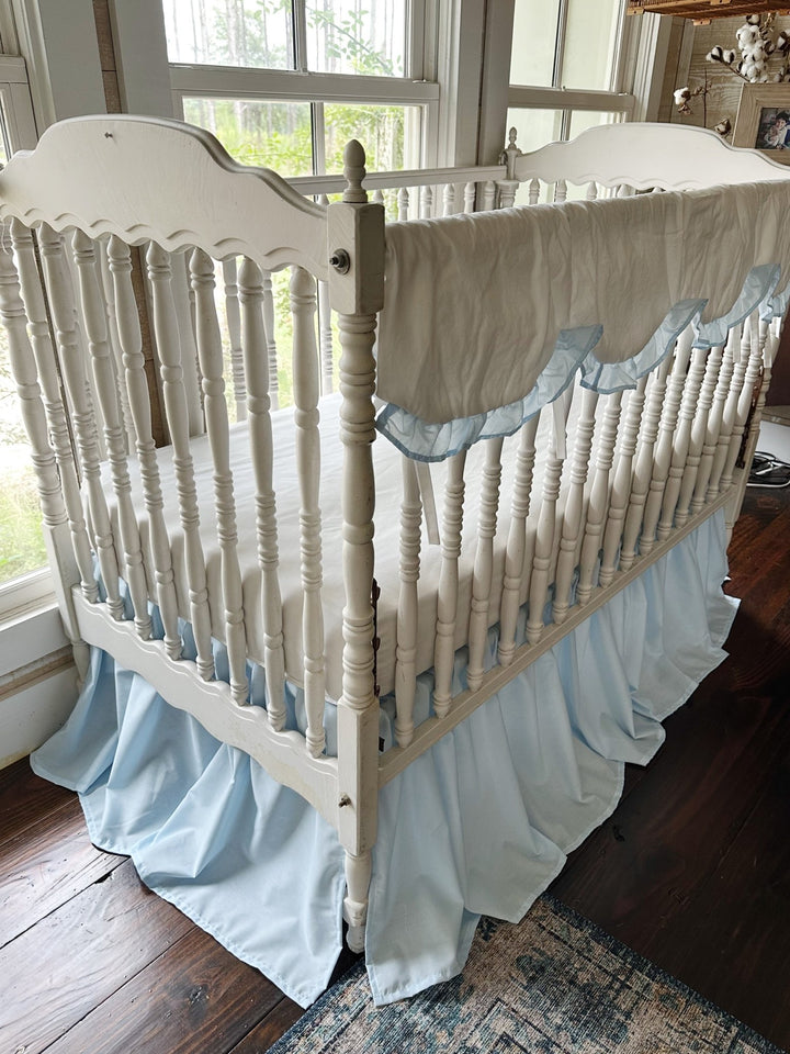 Three quarter view of the crib showing the scalloped cover along the rail and the skirt falling to the floor