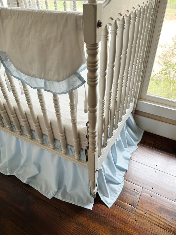 Two piece heirloom blue crib bedding set in a pine-framed nursery with a hanging birdcage