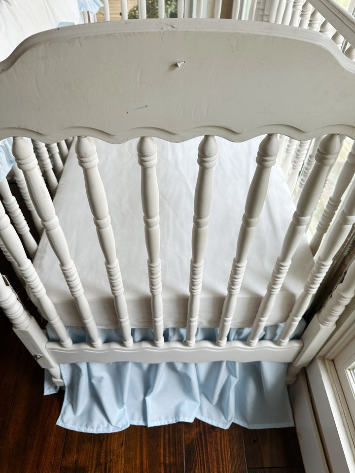 End view of the crib interior showing the white sheet and the heirloom blue skirt hem