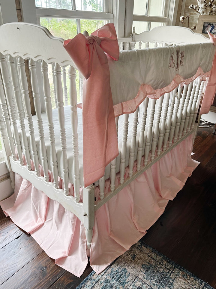 Angled view of a Sisters Pink crib bedding set with a large pink crib bow tied to the corner post