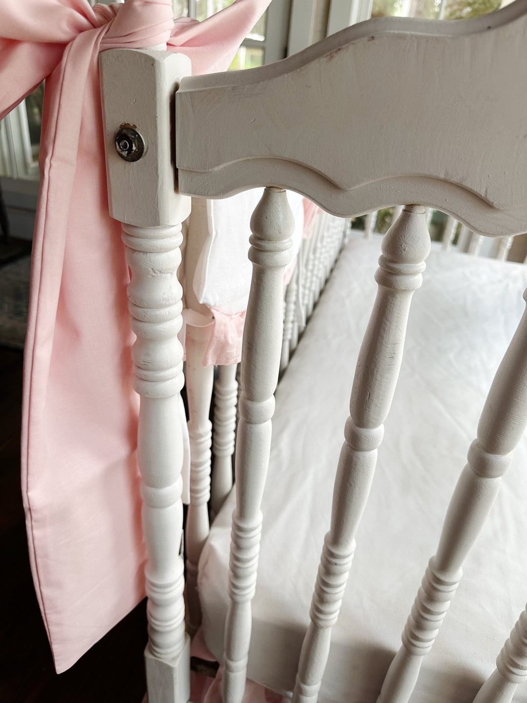 Large Sisters Pink cotton crib bow tied in a full knot at the corner of a white crib