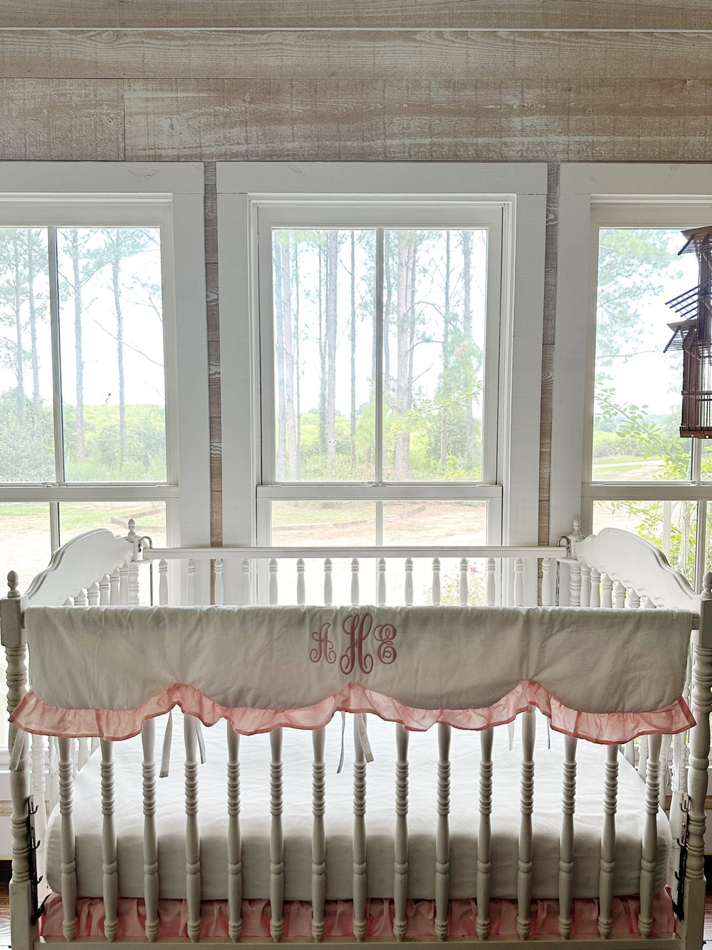 White scalloped crib rail cover with a Sisters Pink ruffle and pink monogram on a white spindle crib