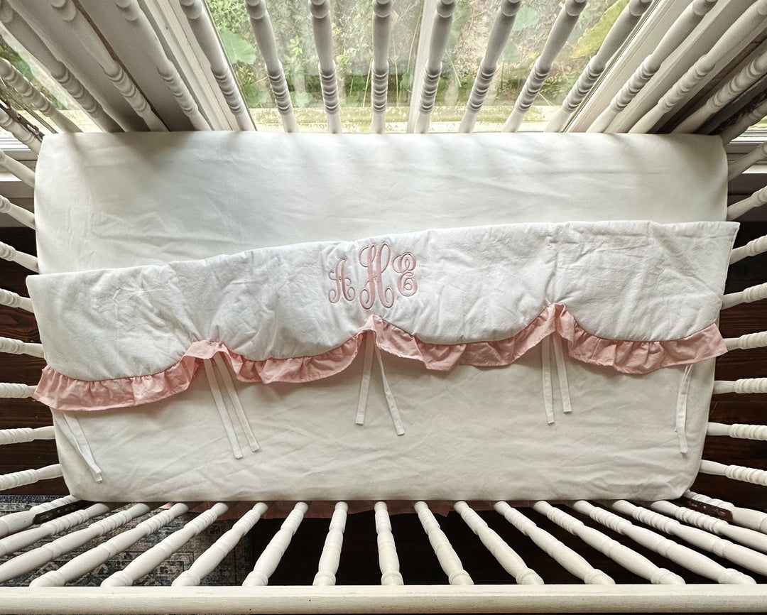 White and Sisters Pink scalloped crib rail cover laid flat, showing its full length, pink ruffle and white cotton ties