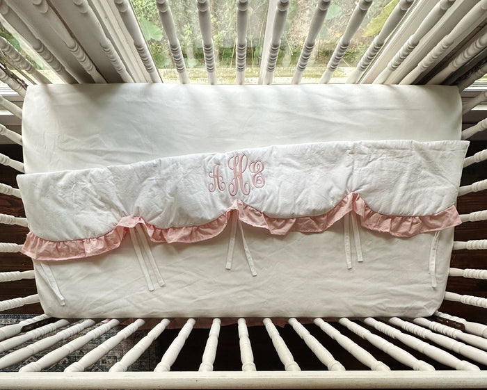 White and Sisters Pink scalloped crib rail cover laid flat, showing its full length, pink ruffle and white cotton ties