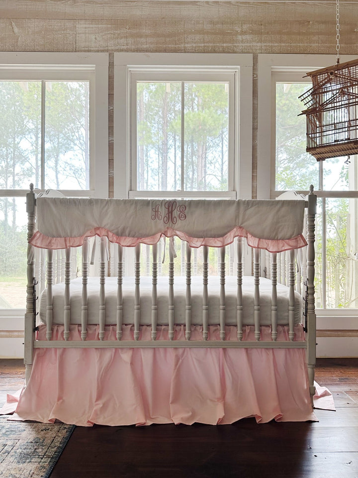 White spindle crib styled with a Sisters Pink scalloped rail cover and farmhouse crib skirt in a bright farmhouse nursery