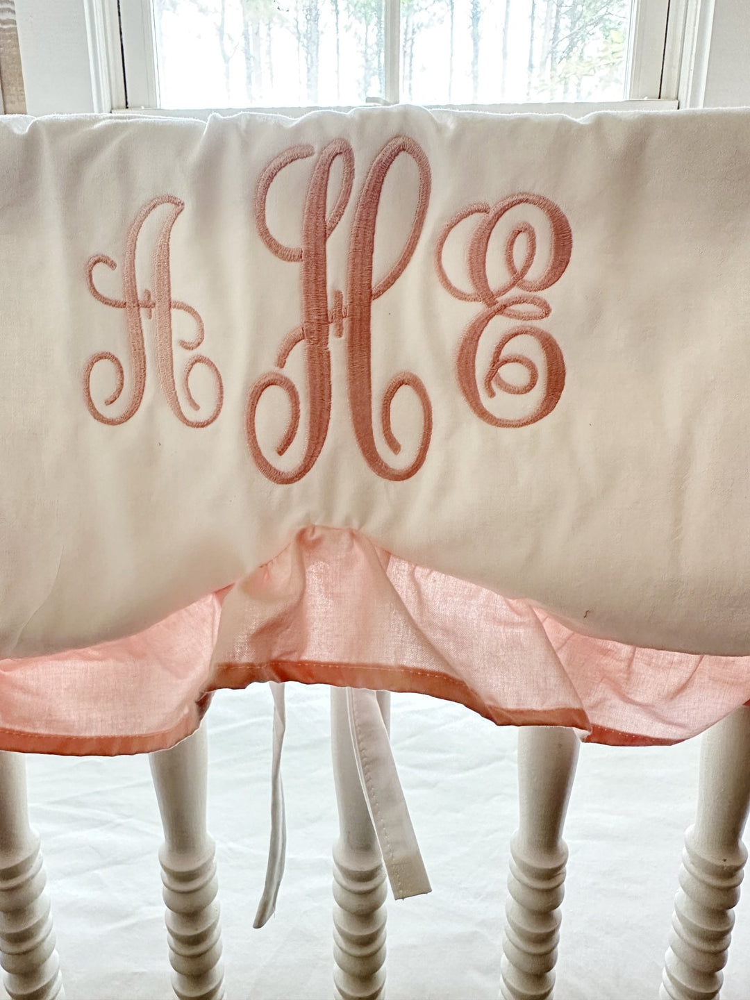 Pink three-initial script monogram embroidered on a white cotton scalloped crib rail cover