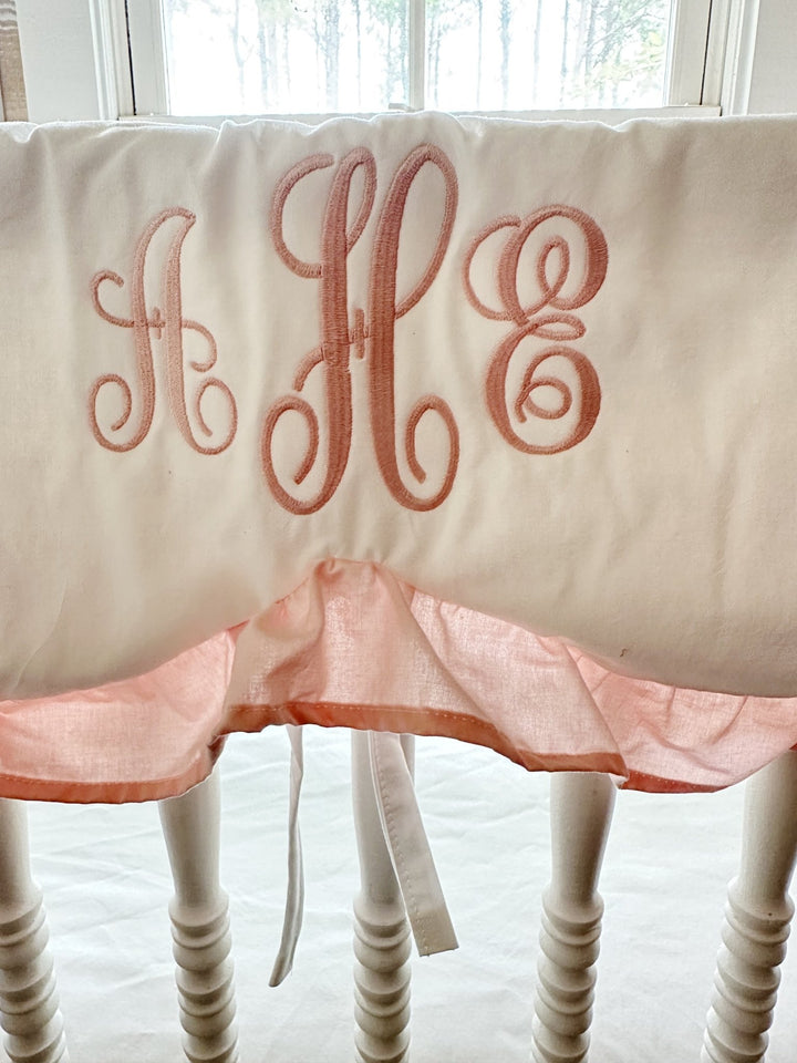 Pink three-initial script monogram embroidered on a white cotton scalloped crib rail cover
