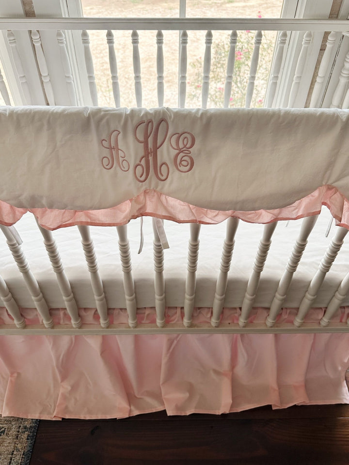 Scalloped crib rail cover with a pink script monogram and Sisters Pink ruffle above a gathered pink crib skirt