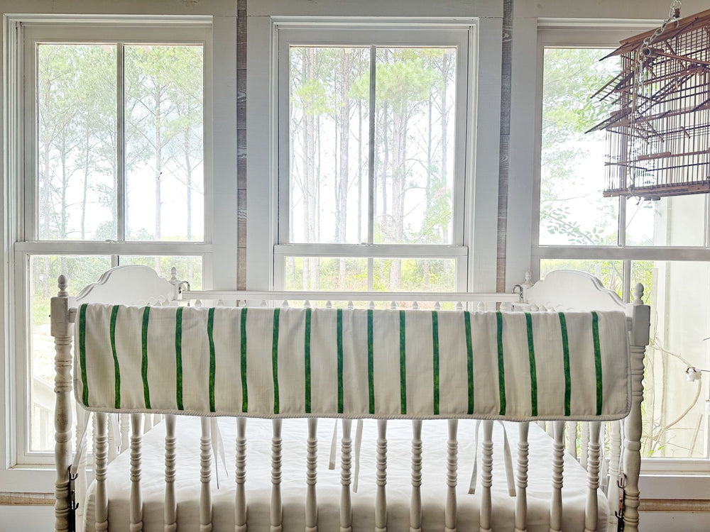 The striped rail cover draped along the top rail of a white Jenny Lind style crib