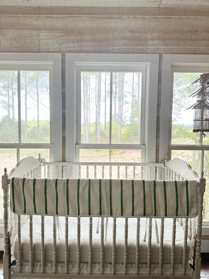 The striped rail cover on a crib in a pine-paneled nursery with windows and a hanging birdcage