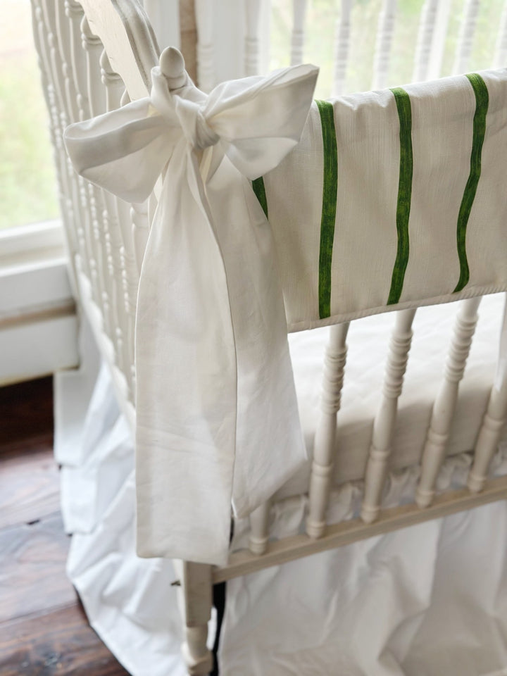 Large white bow knotted over the crib finial beside the green striped rail cover