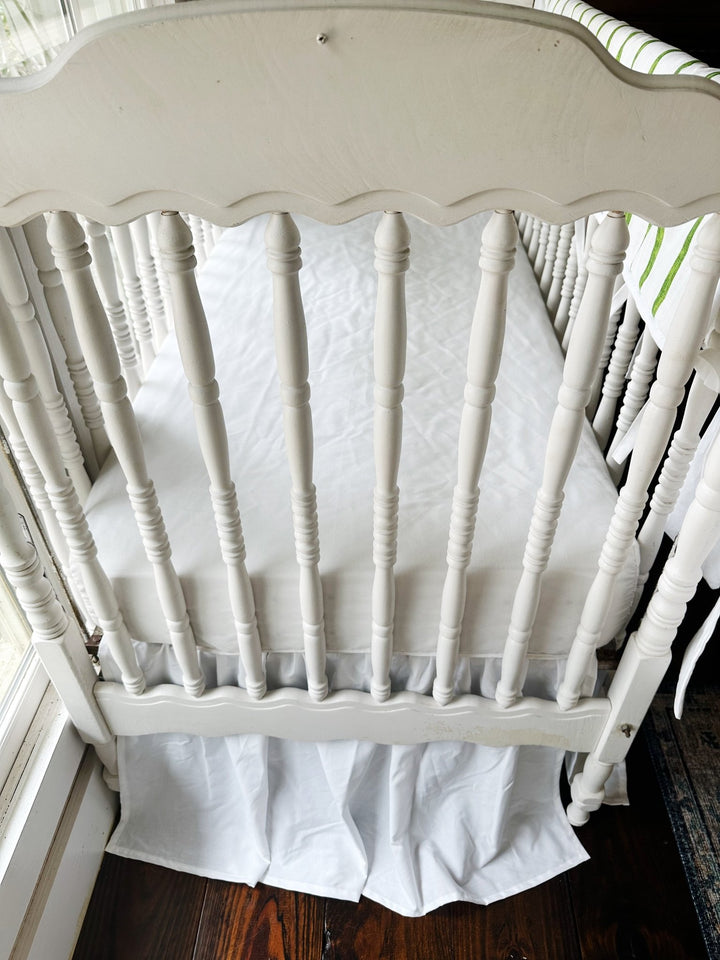 Overhead view from the end of the crib showing the white skirt gathers and crisp white sheet