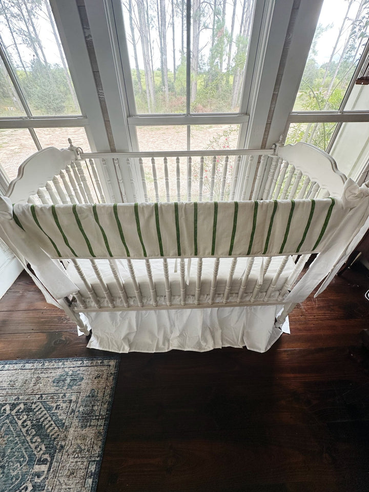 Looking down into the crib at the striped rail cover, white sheet and gathered white skirt