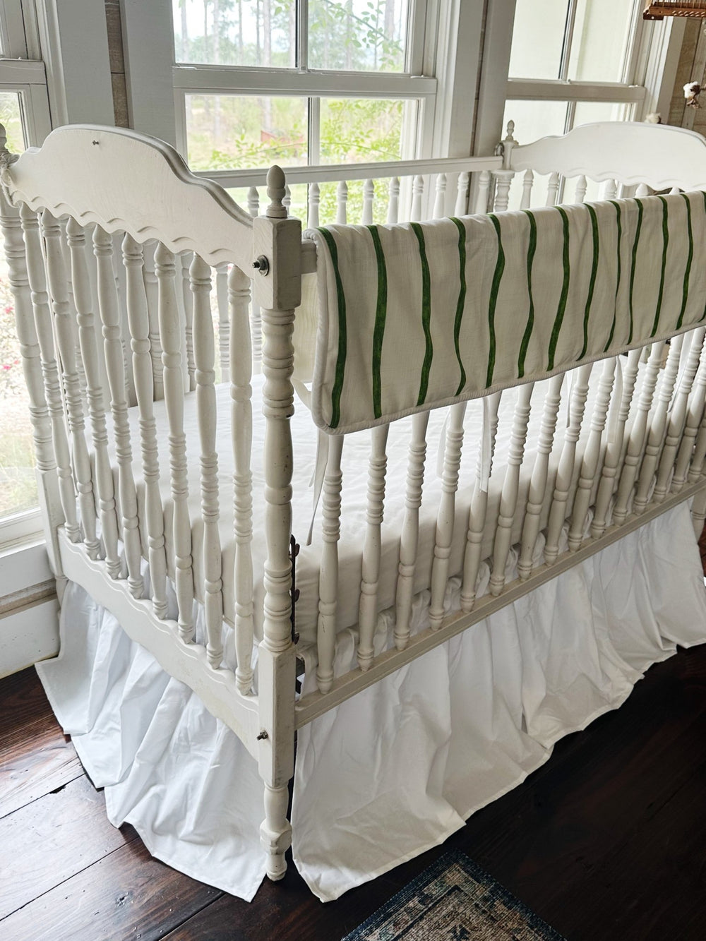 Corner view of the striped rail cover running down the long side of a white spindle crib
