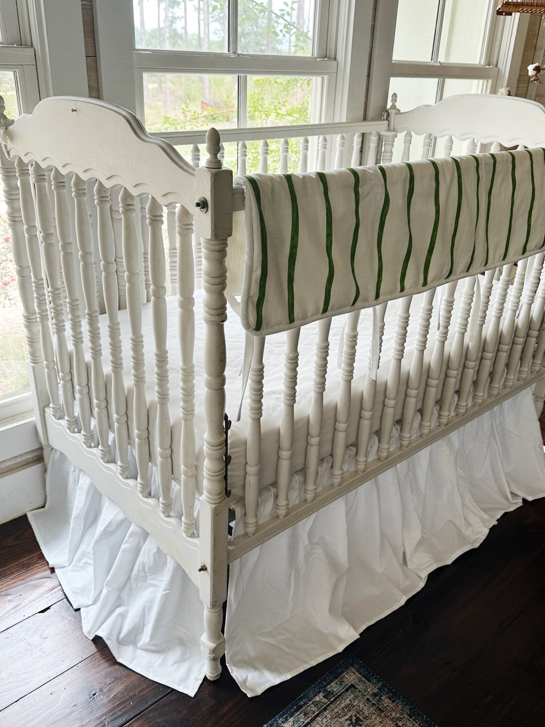 Corner view of the striped rail cover running down the long side of a white spindle crib