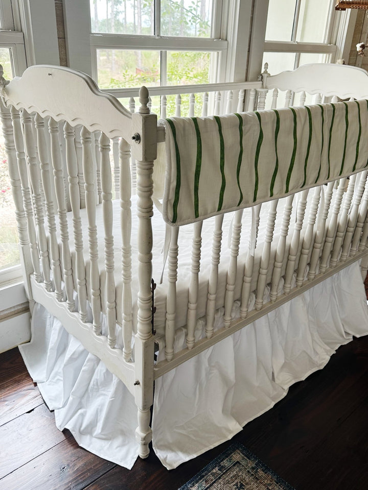 Corner view of the striped rail cover running down the long side of a white spindle crib