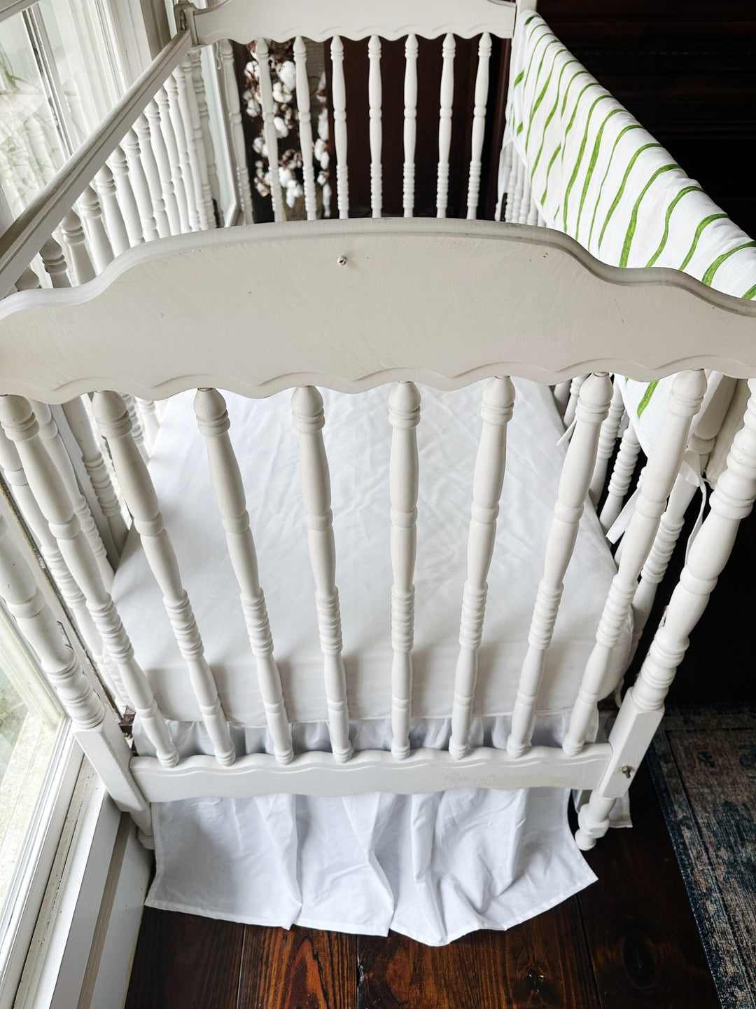 Looking down past the scalloped headboard at the white sheet and gathered skirt