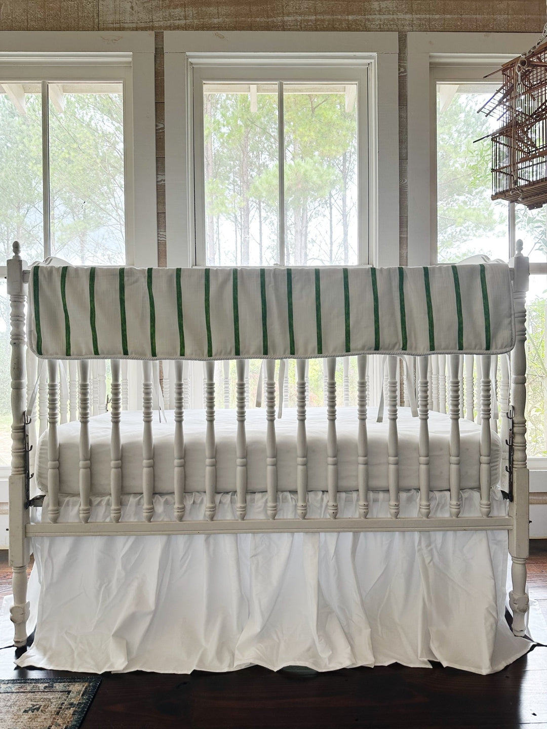 Green and white striped tailored crib rail cover above a gathered white farmhouse crib skirt, no bows on the posts