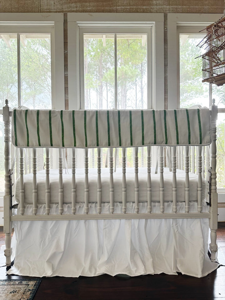 Green and white striped tailored crib rail cover above a gathered white farmhouse crib skirt, no bows on the posts