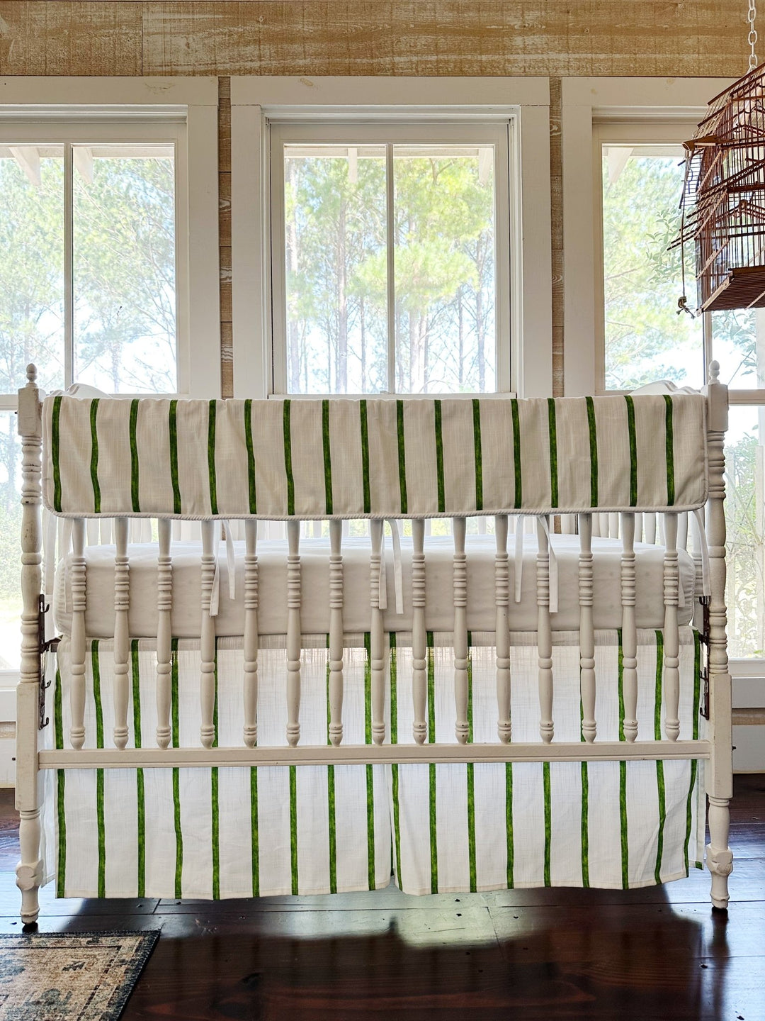 Green and white striped tailored crib rail cover with a matching striped tailored skirt on a white spindle crib