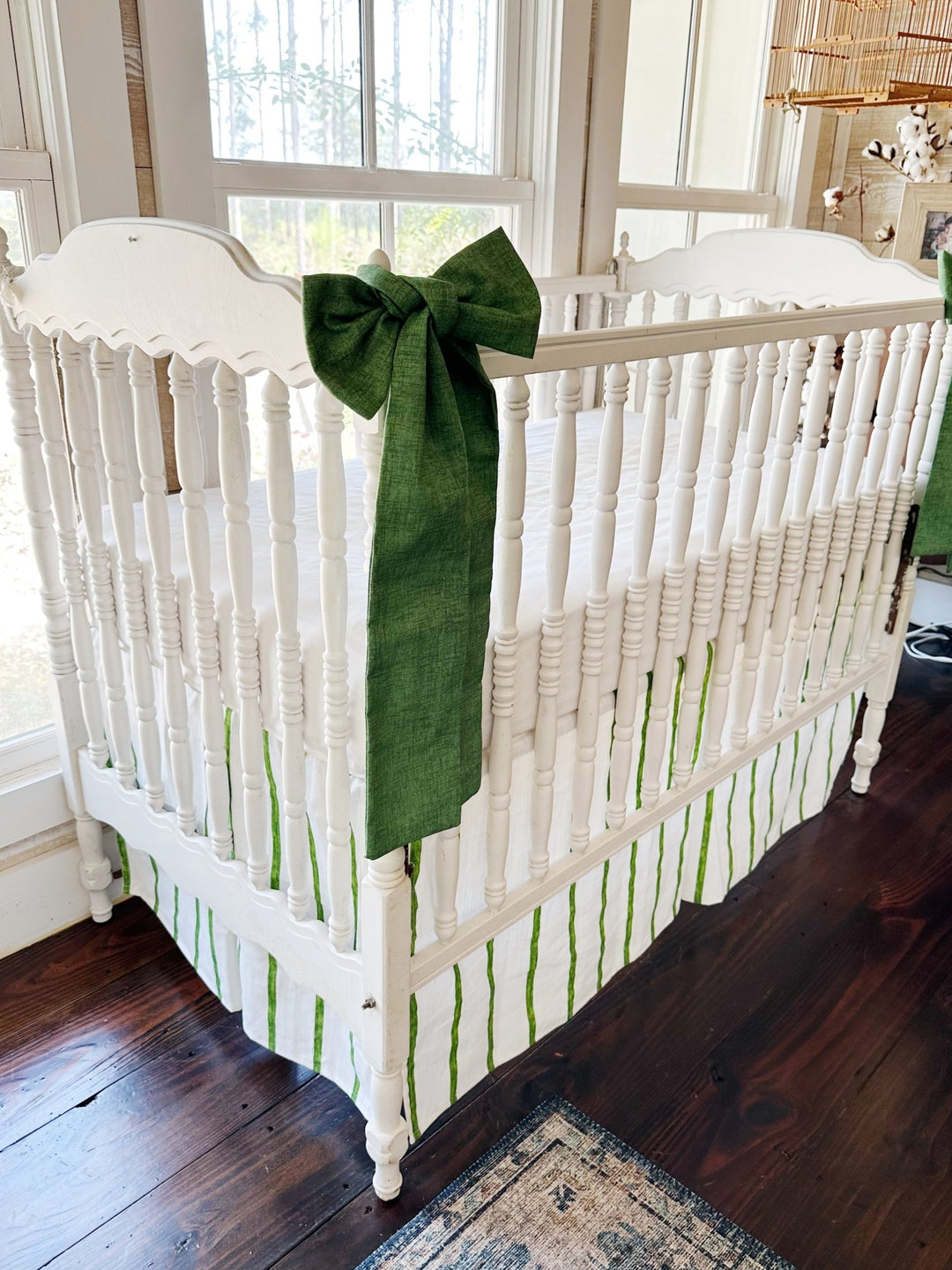 Angled view of the crib showing one green sash and the striped skirt running below the spindles