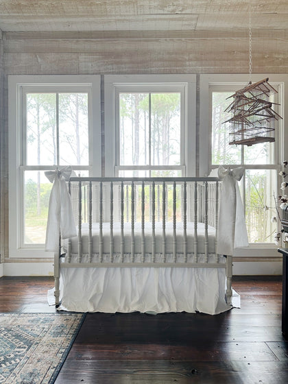 All-white crib skirt and bow set on a Jenny Lind style crib, seen from the corner