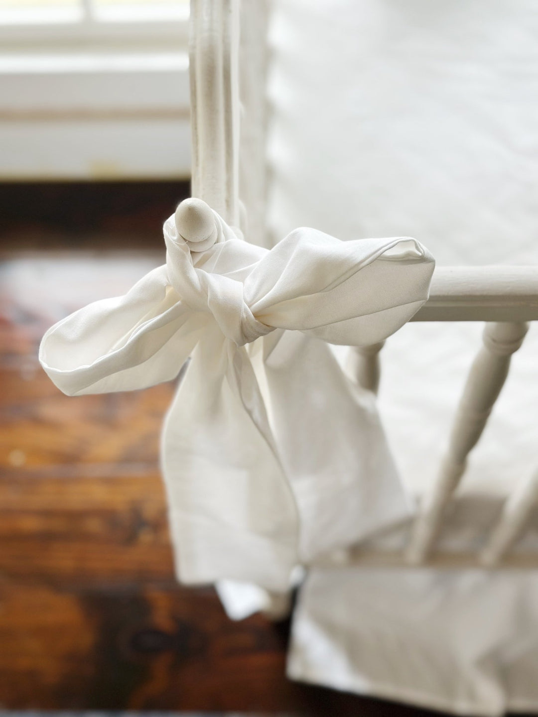 Close view of a large white bow knotted over the crib finial, tails falling long
