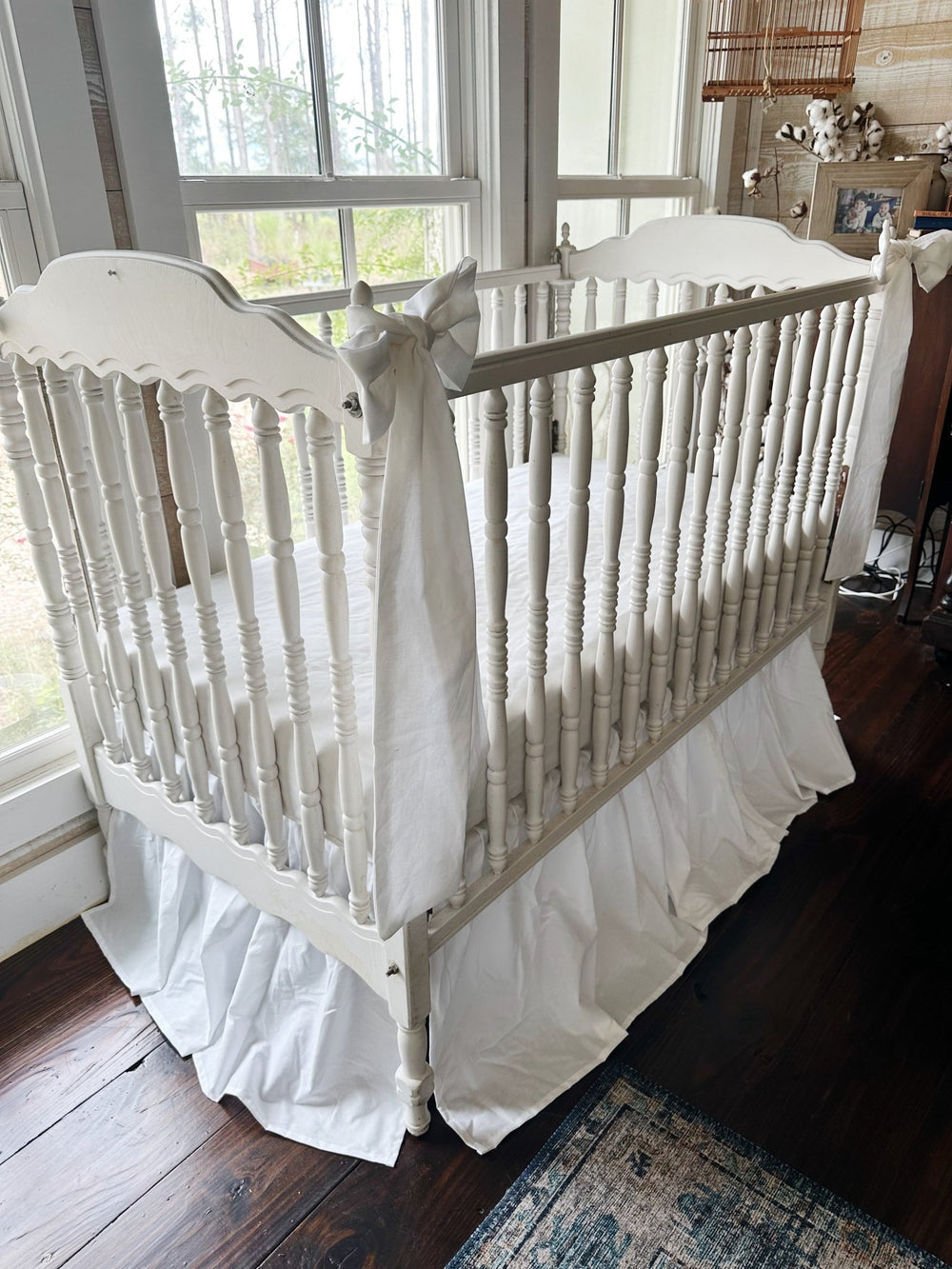 White farmhouse crib skirt with two large white bows tied to the front posts of a spindle crib