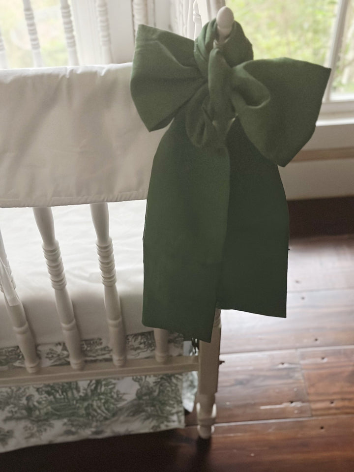 Large cypress green bow tied to a crib post beside the white tailored rail cover