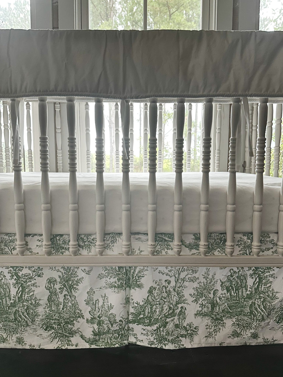 Finished end of the white tailored rail cover where it wraps the crib post, white ties hanging loose