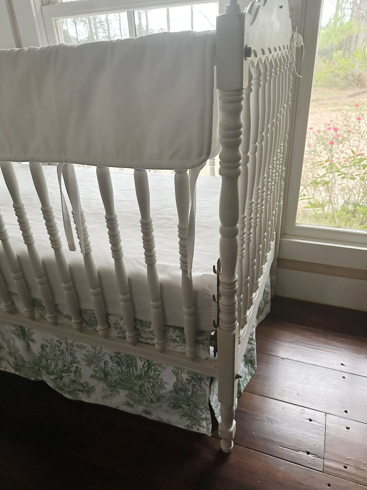 Close view of the white rail cover's cording and ties above the green toile skirt's pastoral print