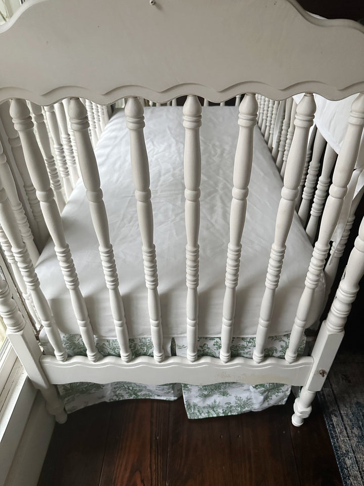 Looking down into the crib at the white fitted sheet with the toile skirt visible below the platform