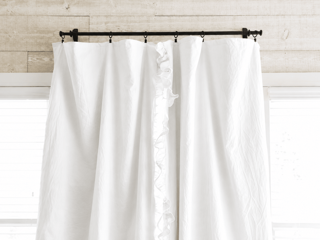 Top of the white curtain panels on a black iron rod with clip rings against whitewashed shiplap - High Cotton Textile
