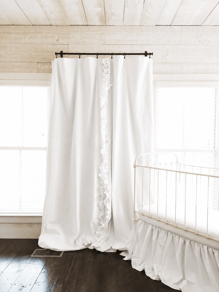 Full length white blackout curtains from rod to floor in a shiplap nursery with a white iron crib - High Cotton Textile